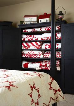 a bed with red and white quilts on top of it next to black cabinets