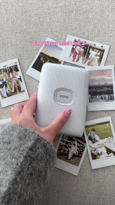 a person holding an electronic device in their hand with pictures on the table behind it