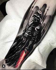 a man with a star wars tattoo on his arm holding a red light saber and darth vader helmet