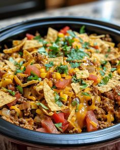 a crock pot filled with taco salad and tortilla chips, garnished with cilantro