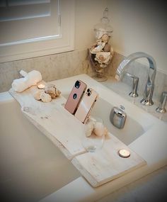 an iphone is sitting on a wooden tray in the bathtub with candles and soap