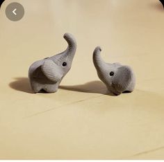 two small elephant figurines sitting on top of a wooden floor next to each other