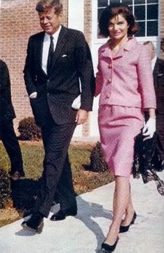 an old photo of two people in suits and ties walking down the sidewalk with one woman