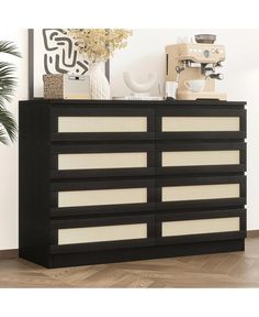 a black and white dresser with drawers next to a plant