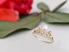 Pearl Crown Ring PRODUCT INFORMATION DETAİLS *Metal Type: Solid 8K/14K/18K (White/Yellow/Rose) Gold *Center Gemstone: White (Pearl quality freshwater pearls with very high luster and smooth surface.) *Ring Band Width : 1 mm *Pearl Size: 6*5 mm *Ring Weight: 2,30 Gram *Standard Ring Size: 7 *Side Stones: 1.10 mm (20 pieces) - 1.50 mm(3 pieces)  Optional Diamond *Quality: VS1 - SI *Carat: 0.45 ct *Colour: E - F  GIFT  ❥ Your product will be sent in a nice high quality jewelry box. ❥ If you have a gift note at the time of purchase, I will be happy to write it on the card. ❥ And there is more than that! I will also send you a gift, a silver jewelry, which is handmade in my atelier. Oh, this would be a surprise!       RETURN POLICY ❥ Item will be produced according to the color and size you cho Yellow Gold Rings For Anniversary Gift, Elegant Ring For Anniversary Gift, Yellow Gold Pearl Ring With Diamond Accents As Gift, Heirloom Pearl Ring With Diamond Accents As Gift, Gold Pearl Ring With Diamonds As Gift, Gold Pearl Ring With Halo Setting For Gift, Elegant Hallmarked Rings For Anniversary Gift, Elegant White Rings For Anniversary Gift, Gold Pearl Ring With Diamonds For Gift