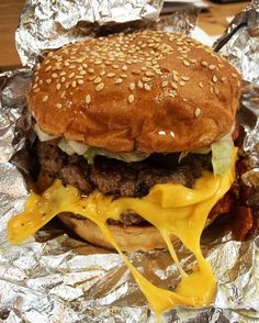 a hamburger with cheese and lettuce on it sitting on tin foil covered table