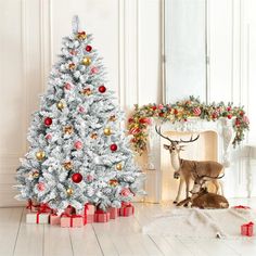 a white christmas tree with red and gold ornaments next to a fireplace in a living room