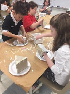 some kids are sitting at a table making cakes