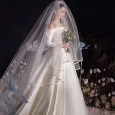 a woman in a white wedding dress and veil walking down the runway with flowers behind her