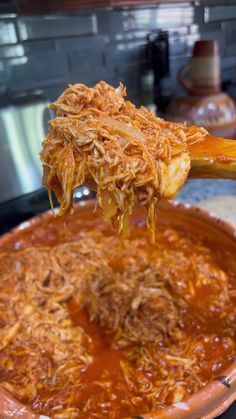 a spoon full of shredded meat being lifted from a casserole dish in a kitchen