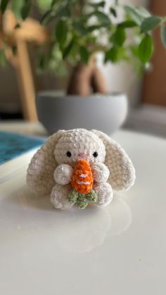 a small crocheted bunny holding a carrot in it's mouth on a table