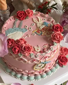 there is a pink cake decorated with roses on the table next to other flowers and figurines