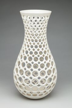 a white vase with holes in it sitting on a table next to a gray wall