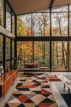 a living room filled with furniture and lots of glass windows overlooking the woods in autumn