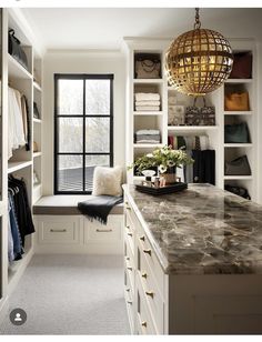 an organized walk - in closet with marble countertops and white cabinets, along with a window seat