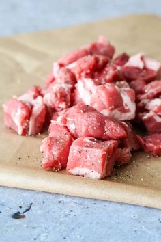 cubes of raw meat sitting on top of a wooden cutting board with seasoning