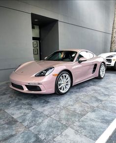 a pink porsche sports car parked in front of a building with two other cars behind it