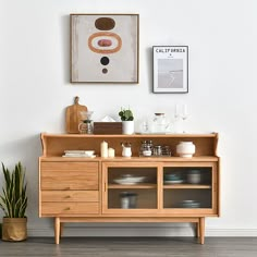 a wooden cabinet sitting next to a painting and potted plant on top of a hard wood floor