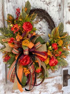 a wreath is hanging on the front door with flowers and leaves around it, as well as an orange ribbon