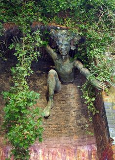 a statue is sitting in the middle of some bushes and ivys, with one hand on his head