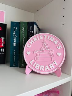 there is a pink sign that says christmas library on the shelf next to some books