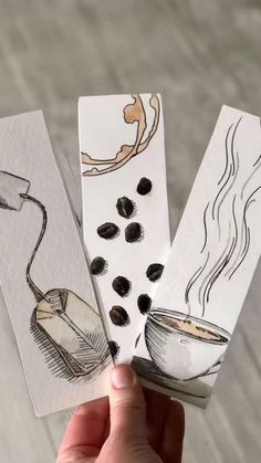 three handmade bookmarks with coffee drawings on them, one being held in the air