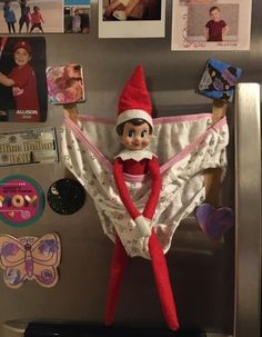 an elf is hanging on the refrigerator door with pictures and magnets all around it