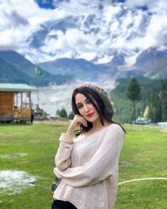 a woman standing on top of a lush green field next to a mountain covered in snow