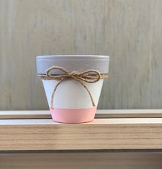 a white and pink flower pot with a brown string tied around the top on a wooden table