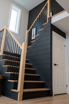 a staircase with black painted walls and wooden handrails in an empty room next to a white door