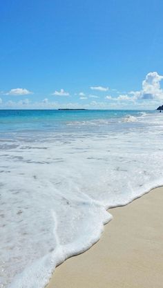 an ocean beach with waves coming in to the shore and blue sky above it on a sunny day