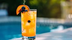 a tall glass filled with orange juice next to a swimming pool