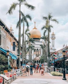 people are walking down the street in front of some buildings and palm trees on a cloudy day