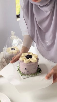 a woman is decorating a cake with bananas and blueberries on it while wearing a hijab