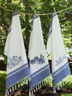 three blue and white towels hanging on a clothes line in front of a tree with green leaves