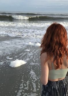 a woman standing on top of a beach next to the ocean with waves coming in