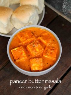 a bowl filled with tofu and bread on top of a wooden table next to rolls