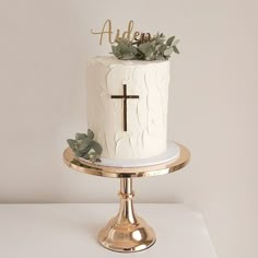 a white cake with greenery on top sits on a gold stand