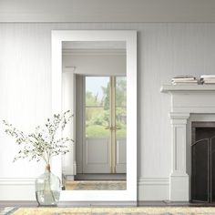 a living room with a fireplace, mirror and vase filled with flowers on the floor