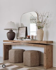 a wooden table with two stools and a mirror on the wall above it in a white room