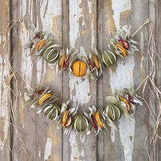 a wreath made out of leaves and oranges on a wooden background with peeling paint