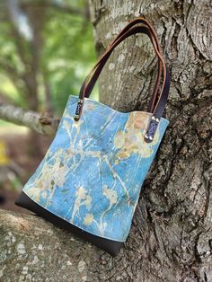 "Lovely, one of a kind handbag! Designed with leaves and plants ecoprinted onto Leather! Hand crafted  in my NC studio. This unique pale blue handbag showcases my ecoprinted (botanical) designs on both the exterior and interior of the bag. I combined it with a rich brown leather as a contrast on the boxed bottom, and two 1/2\" wide handles. The bag is 12\" high x 11\" wide by 3\" deep. It's a perfect size for carrying your essentials.  Handcrafted by me and finished with stylish silver rivets. Can be carried over the arm or ticked up under the shoulder. I ecoprint on both fabric and leather and the results are one of a kind. I collect various leaves and foliage from my NC farm and through a natural process, imprint them onto leather. I handcraft the hides into handbags, journals, accessori Artistic Blue Shoulder Bag For Everyday Use, Artistic Blue Bag For Everyday Use, Nature-inspired Rectangular Bag For Daily Use, Everyday Nature-inspired Rectangular Bag, Nature-inspired Everyday Rectangular Bag, Artistic Blue Bags For Everyday, Handmade Nature-inspired Bag For Daily Use, Nature-inspired Handmade Shoulder Bag For Everyday Use, Nature-inspired Handmade Bags For Everyday Use