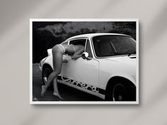 a black and white photo of a woman leaning on a car