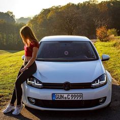 a woman sitting on the hood of a white car in front of a grassy field