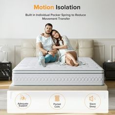 a man and woman sitting on top of a white bed in front of a wall with an advertisement for motion isolation