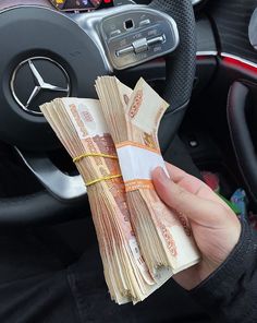 a person holding money in their hand next to a steering wheel