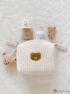 a white purse with teddy bears and other items on it sitting on a bed next to a baby's pacifier