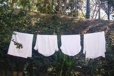 three white towels hanging on a clothes line in front of some trees and bushes,