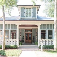 a white house with blue shutters on the front and side windows, along with palm trees