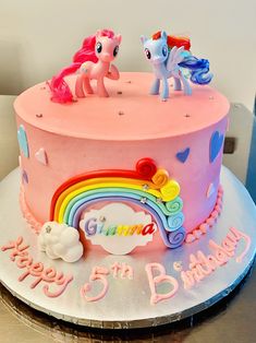 a pink birthday cake decorated with rainbows and ponies